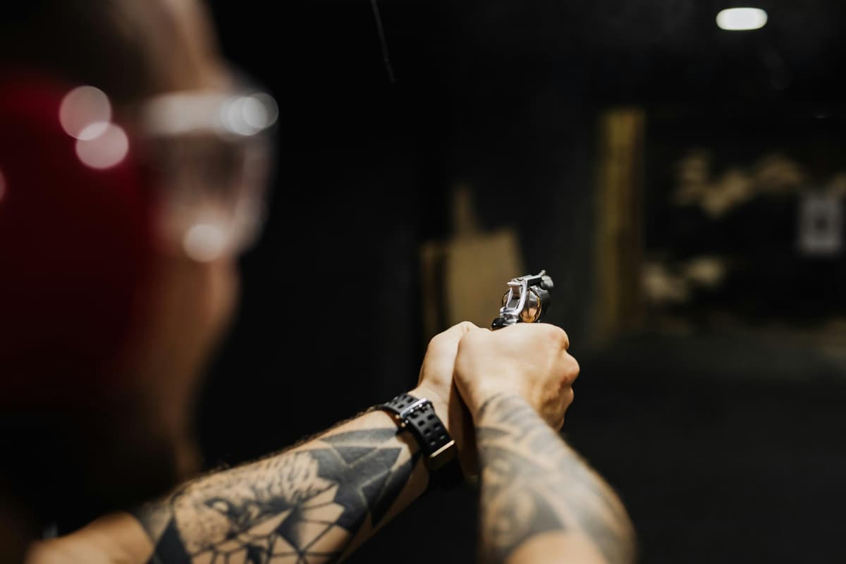 Person with tattoos aiming a revolver at an indoor shooting range